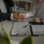 two people shaking hands over a piece of paper