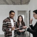 A diverse couple signing documents with a realtor in a new home setting.