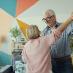Elderly couple dancing happily in a colorful living room.
