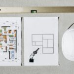 Blueprints, spirit level, and hard hat symbolize house planning.
