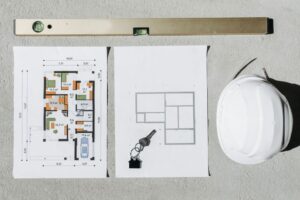 Blueprints, spirit level, and hard hat symbolize house planning.