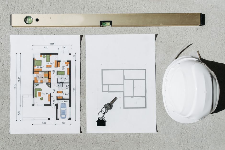 Blueprints, spirit level, and hard hat symbolize house planning.